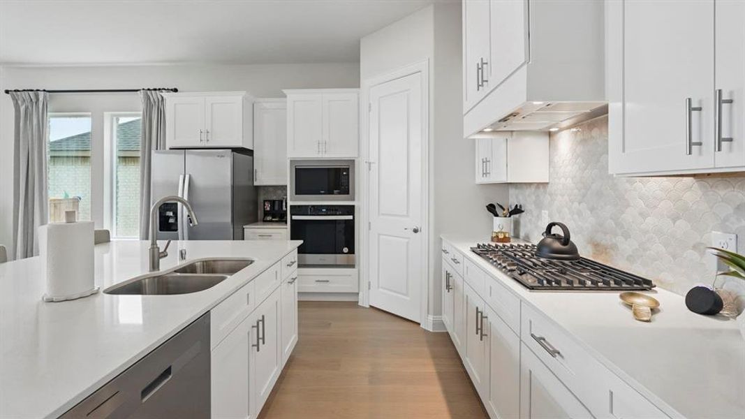 Kitchen featuring white cabinets, stainless steel appliances, light wood-type flooring, light stone counters, and decorative backsplash
