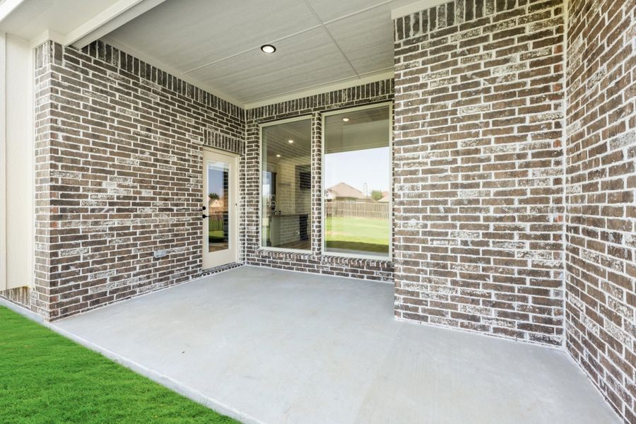 Covered back patio with concrete floor, brick walls, and sliding glass door leading to backyard