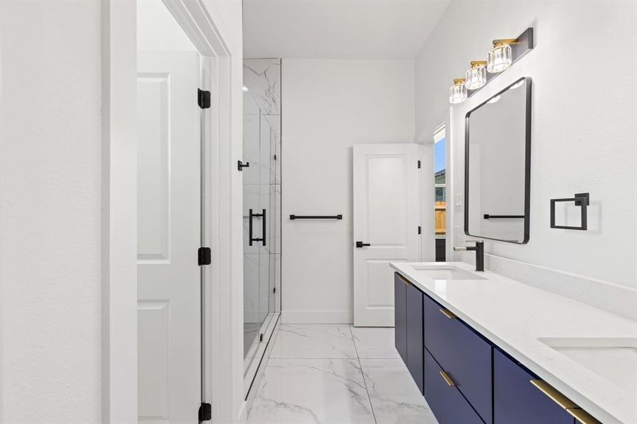 Full bath featuring a marble finish shower, double vanity, and light marble finish floors