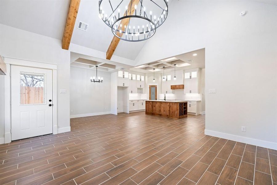 Unfurnished living room featuring an inviting chandelier, sink, beam ceiling, and high vaulted ceiling