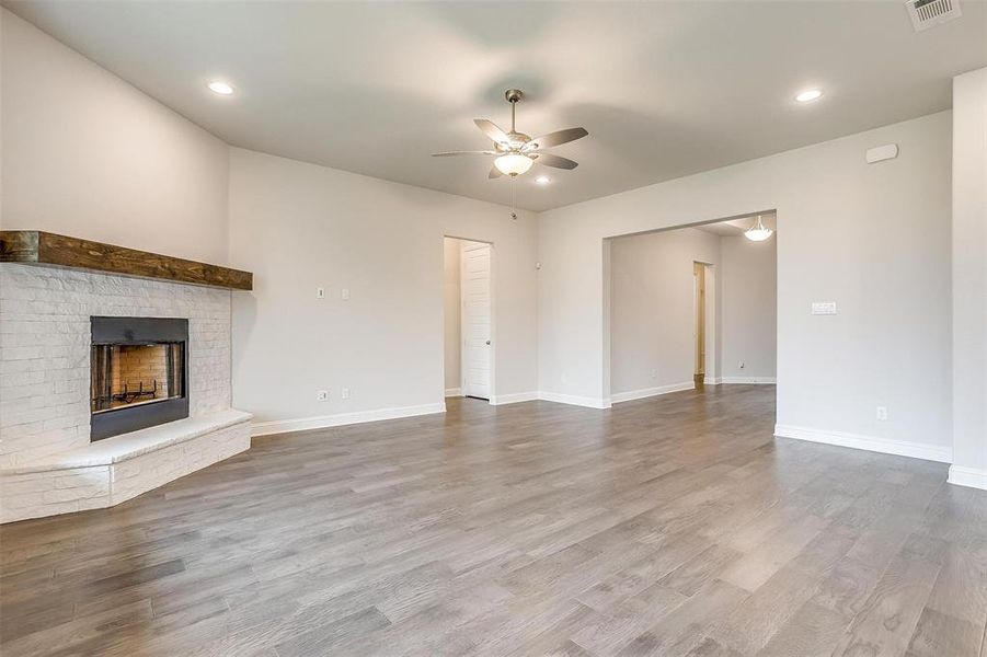 Unfurnished living room with wood-type flooring, a brick fireplace, and ceiling fan