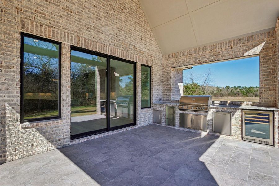 This outdoor space features a covered patio with a built-in grill and fridge, surrounded by brick walls.
