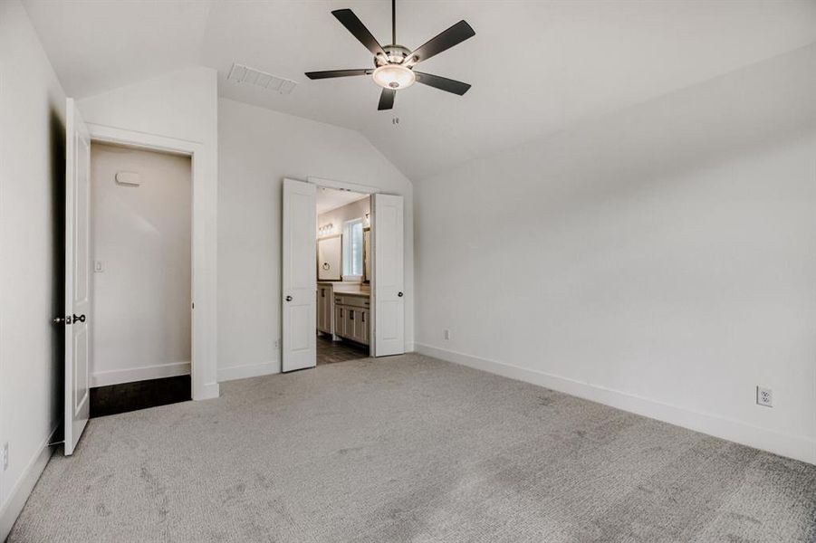 Unfurnished bedroom with connected bathroom, vaulted ceiling, light colored carpet, and ceiling fan