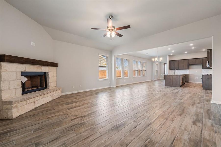 Unfurnished living room with a stone fireplace, a chandelier, a ceiling fan, light wood finished floors, and recessed lighting Unfurnished living room with a stone fireplace, a chandelier, a ceiling fan, light wood finished floors, and recessed lighting