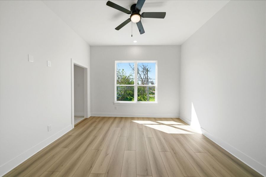 Bright, spacious room with light LVP flooring, large window for natural light, and a ceiling fan. Ideal for a bedroom or home office.