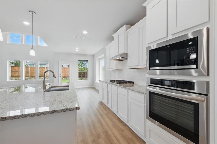 Kitchen with stainless steel appliances, a sink, decorative backsplash, light wood-style flooring, and white cabinets Kitchen with stainless steel appliances, a sink, decorative backsplash, light wood-style flooring, and white cabinets