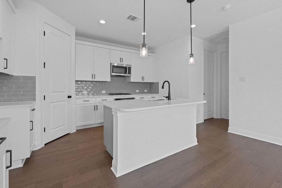 Kitchen with a kitchen island with sink, pendant lighting, tasteful backsplash, dark wood-style flooring, and stainless steel microwave Kitchen with a kitchen island with sink, pendant lighting, tasteful backsplash, dark wood-style flooring, and stainless steel microwave