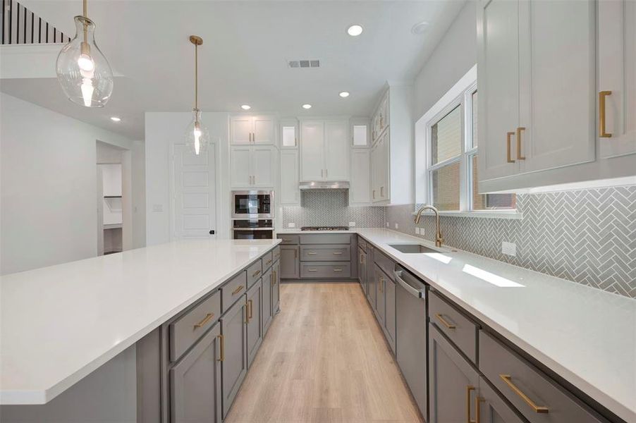 Two tone kitchen featuring two tone cabinetry, pendant lighting, light wood finished floors, stainless steel appliances, and light stone counters