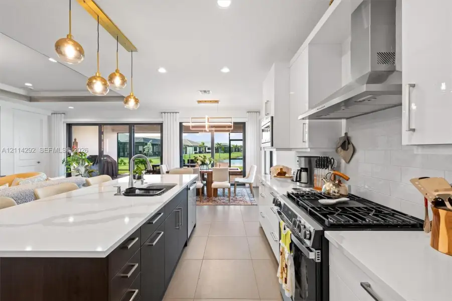 Kitchen featuring a central island with quartz countertops, high-gloss cabinetry, a stainless steel range hood, and pendant lighting