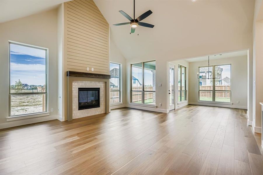Unfurnished living room with high vaulted ceiling, a fireplace, light wood-type flooring, and ceiling fan Unfurnished living room with high vaulted ceiling, a fireplace, light wood-type flooring, and ceiling fan
