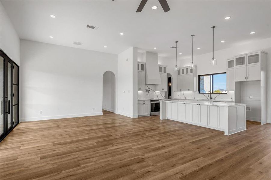 Kitchen with glass insert cabinets, arched walkways, light countertops, white cabinets, and open floor plan