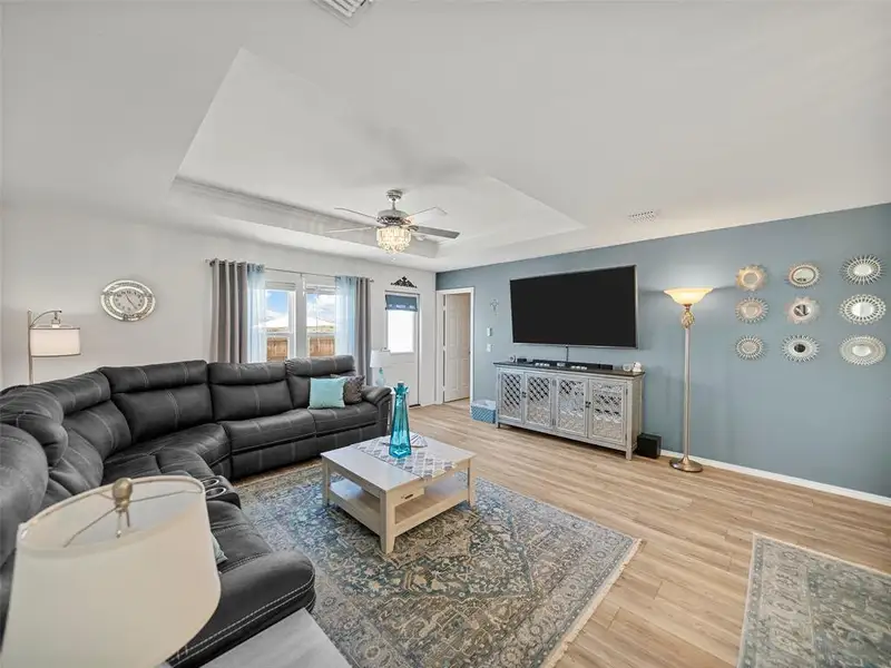Living room featuring a tray ceiling, visible vents, ceiling fan, wood finished floors, and baseboards