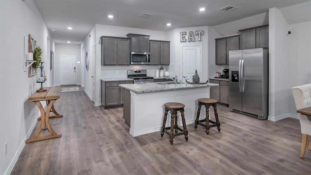 Kitchen featuring appliances with stainless steel finishes, backsplash, light stone countertops, a breakfast bar, and an island with sink Kitchen featuring appliances with stainless steel finishes, backsplash, light stone countertops, a breakfast bar, and an island with sink