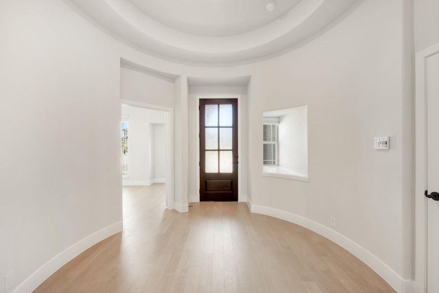 Curved foyer with domed ceiling, light hardwood floors, and dark wood front door with glass panels