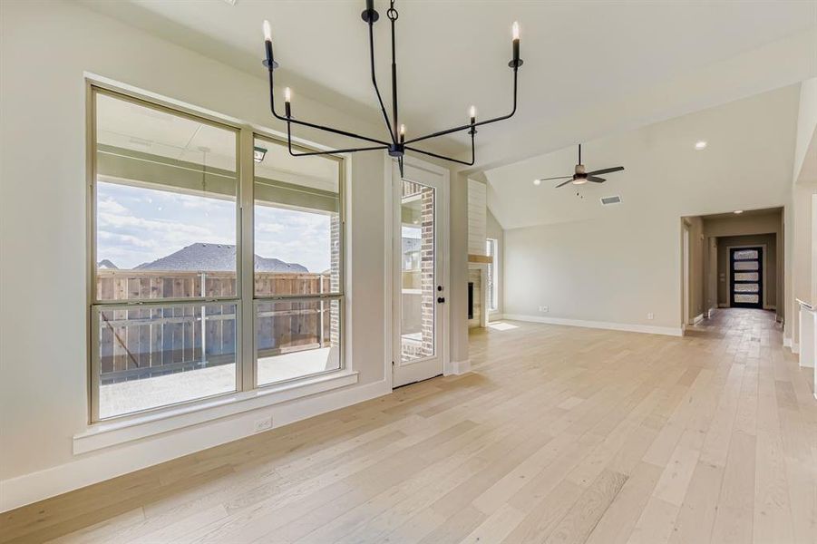 Unfurnished living room featuring light wood finished floors, a chandelier, vaulted ceiling, a fireplace, and a ceiling fan