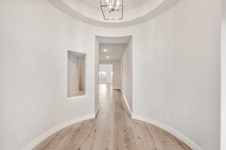 Round foyer with tray ceiling, modern chandelier, wood floors, and hallway leading to main living area