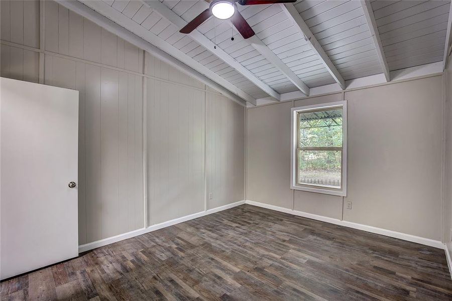 Empty room with lofted ceiling with beams, dark wood-type flooring, ceiling fan, and wood ceiling