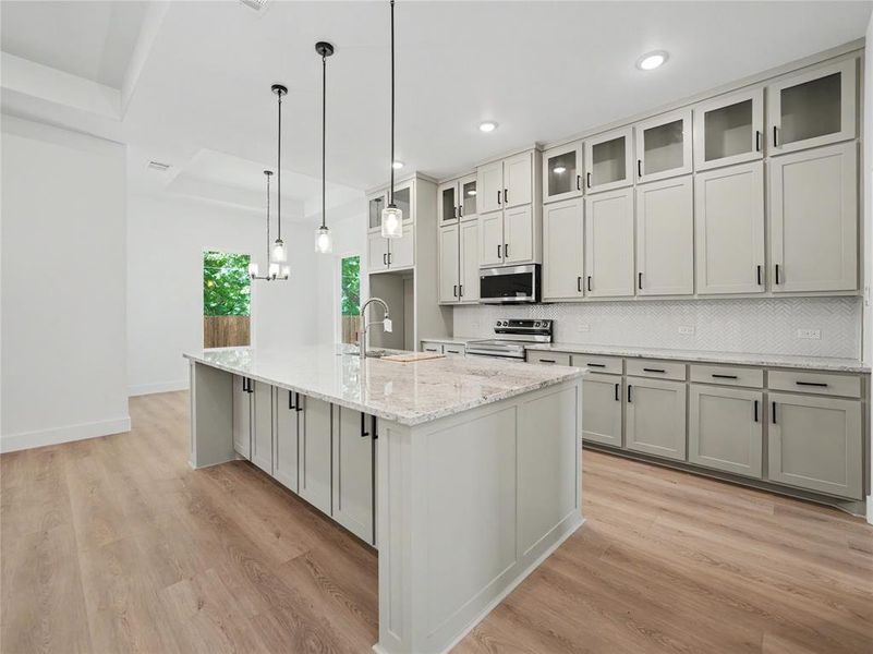 Gourmet kitchen featuring a large island, light-toned cabinetry, granite countertops, wood-finish flooring, and pendant lighting Gourmet kitchen featuring a large island, light-toned cabinetry, granite countertops, wood-finish flooring, and pendant lighting