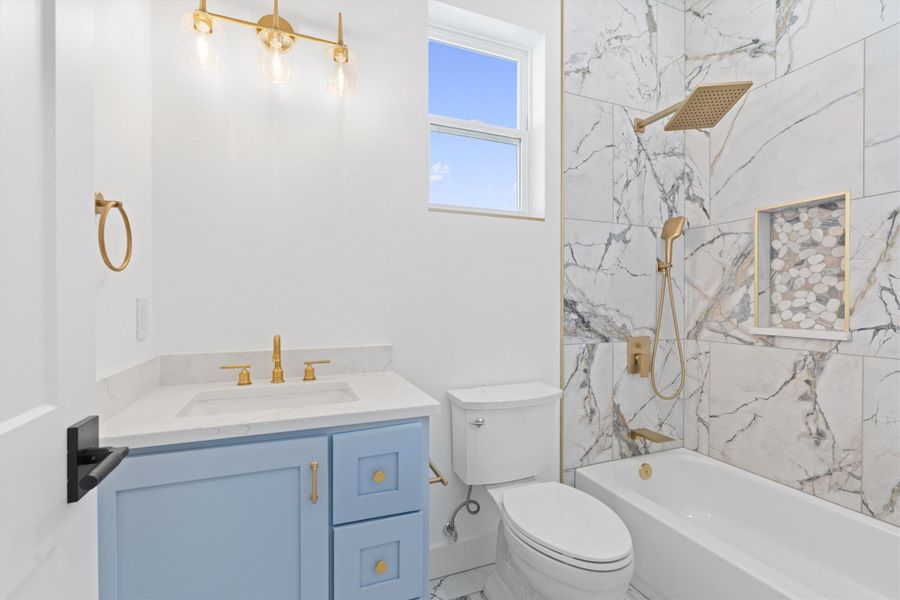Elegant gold fixtures accent a chic blue vanity, complementing the luxurious marble-tiled shower and pristine white bathtub. Elegant gold fixtures accent a chic blue vanity, complementing the luxurious marble-tiled shower and pristine white bathtub.