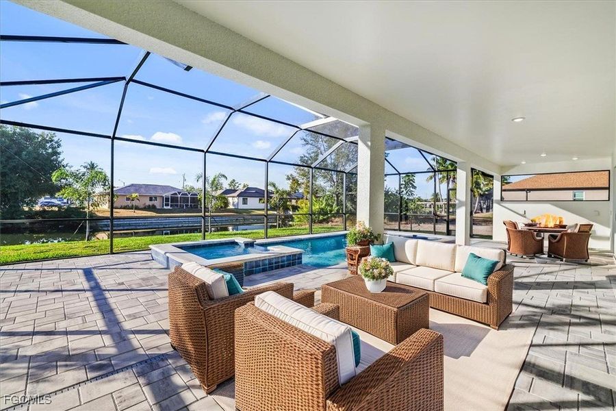 View of patio / terrace featuring a sunroom, glass enclosure, a pool with connected hot tub, a water view, and an outdoor living space