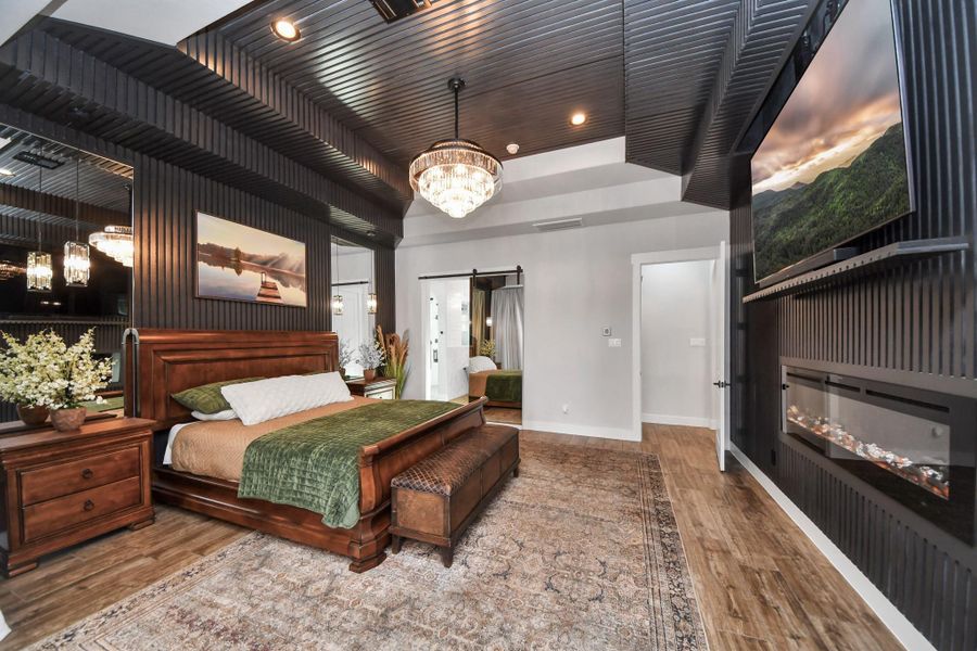 Luxurious bedroom featuring a stunning chandelier, elegant wood accents, and a cozy fireplace under a modern, coffered ceiling.