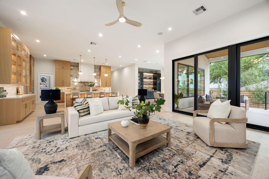 An inviting main living space where open design meets comfort, anchored by wide-plank flooring and soft natural light. Expansive glass doors extend the living area outward, creating a seamless indoor-outdoor experience perfect for entertaining. The layout flows effortlessly into adjacent spaces, offering both flexibility and a sense of connection while maintaining a calm, cohesive aesthetic throughout.
