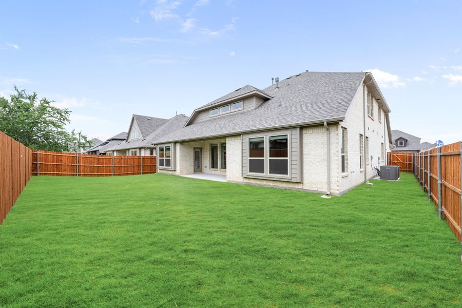 Backyard of two-story brick home with large green lawn, patio, and wood privacy fence