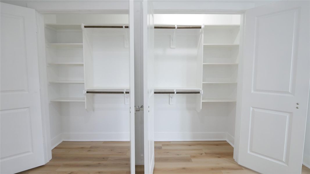 This photo shows a spacious walk-in closet with double doors, featuring multiple shelves and hanging rods, perfect for organized storage. The room has a light, airy feel with white walls and a light wood floor. This photo shows a spacious walk-in closet with double doors, featuring multiple shelves and hanging rods, perfect for organized storage. The room has a light, airy feel with white walls and a light wood floor.