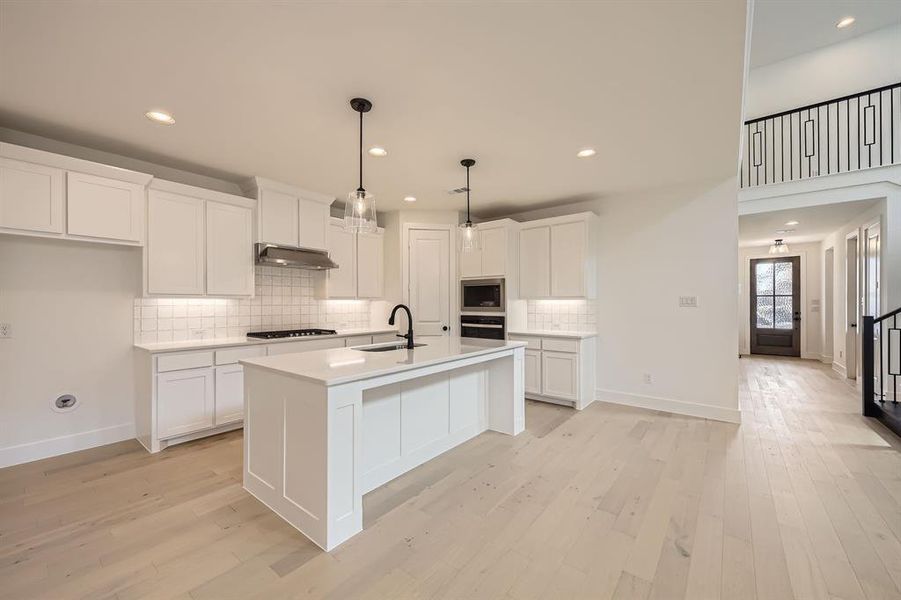 Kitchen featuring white cabinetry, backsplash, light countertops, light wood-type flooring, and recessed lighting Kitchen featuring white cabinetry, backsplash, light countertops, light wood-type flooring, and recessed lighting