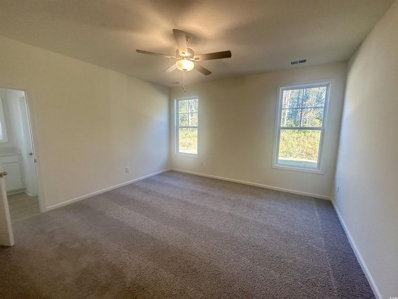 Carpeted empty room featuring plenty of natural light and ceiling fan Carpeted empty room featuring plenty of natural light and ceiling fan