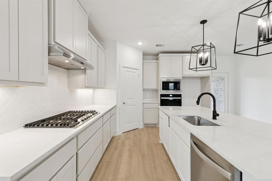 Kitchen with stainless steel appliances, light wood-type flooring, under cabinet range hood, white cabinets, and light countertops Kitchen with stainless steel appliances, light wood-type flooring, under cabinet range hood, white cabinets, and light countertops
