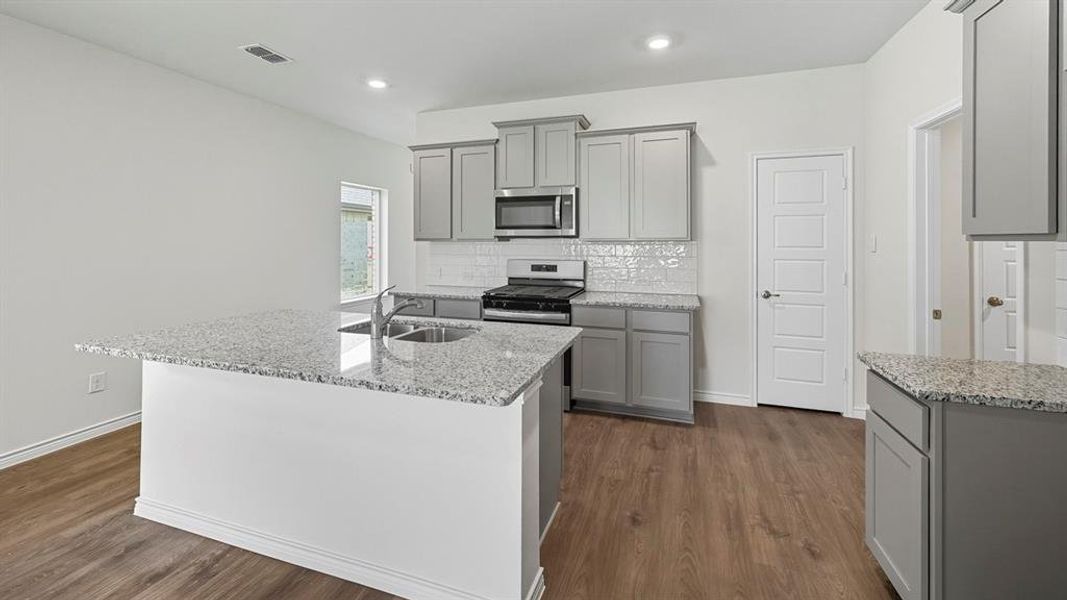 Kitchen with gray cabinetry, backsplash, light stone countertops, stainless steel appliances, and recessed lighting