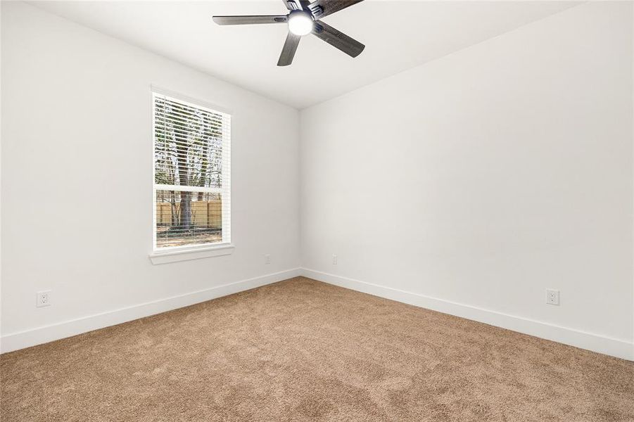 This room features a neutral carpet, white walls, and two large windows offering plenty of natural light. A ceiling fan is centrally located, providing comfort and circulation. Ideal for a cozy bedroom or home office.