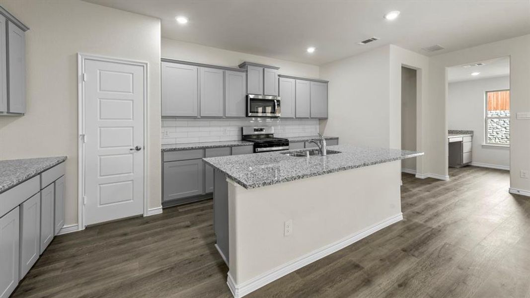 Kitchen featuring grey cabinetry, stainless steel appliances, a white subway tile backsplash, and a large island with a double basin sink and extended countertop