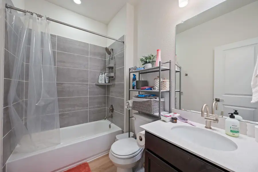 Full bathroom featuring shower / bathtub combination with curtain, vanity, and light wood finished floors Full bathroom featuring shower / bathtub combination with curtain, vanity, and light wood finished floors