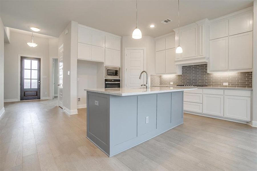 Kitchen featuring appliances with stainless steel finishes, light wood-type flooring, white cabinets, and backsplash