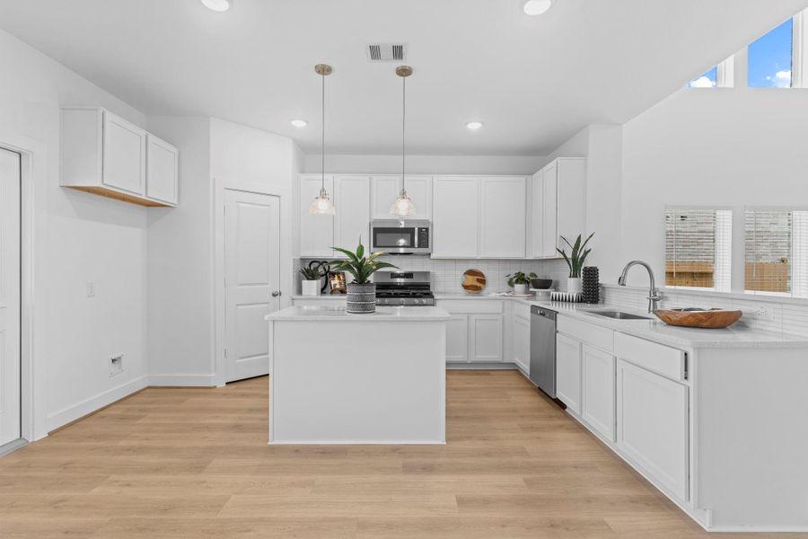 This well-appointed kitchen offers clean lines and modern style, featuring 42” white cabinetry, stainless appliances, a gas range, large center island, and a walk-in pantry—all framed by stylish lighting and woodlike tile flooring. **Image Representative of Plan Only and May Vary as Built**.