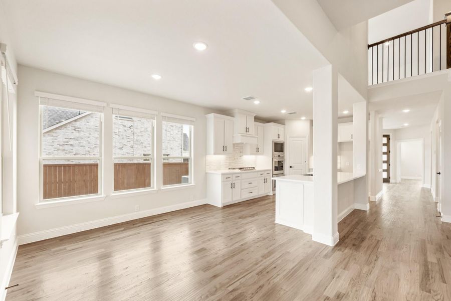 Open-concept living area and kitchen with white cabinets, hardwood floors, and second-floor balcony overlook