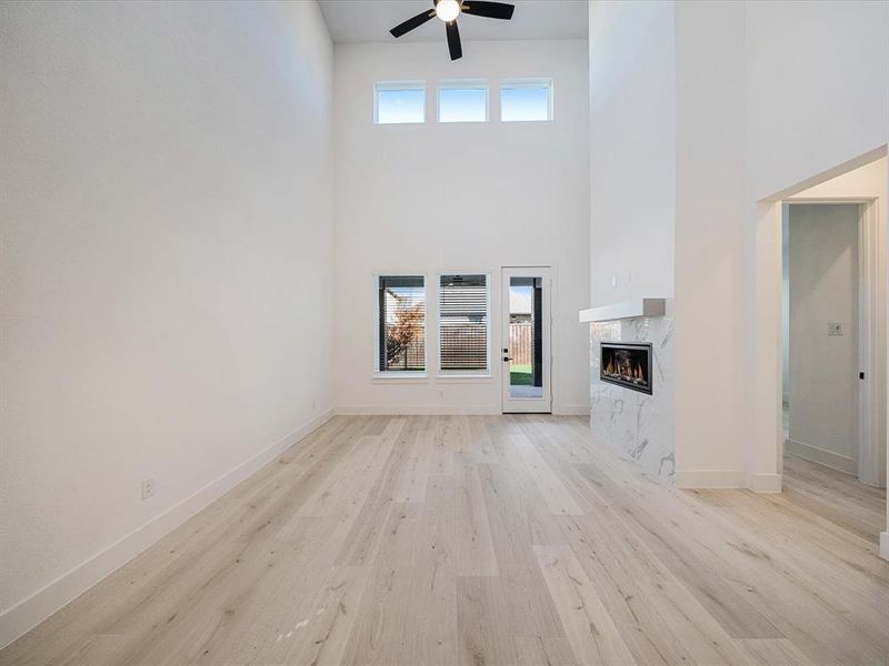 Unfurnished living room with healthy amount of natural light, light wood-type flooring, a high end fireplace, a towering ceiling, and a ceiling fan