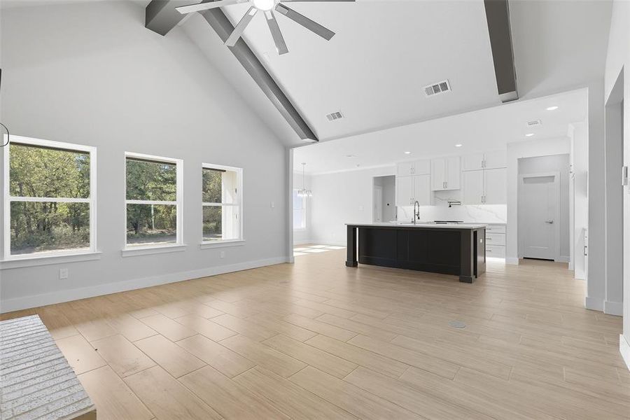 Unfurnished living room featuring high vaulted ceiling, beam ceiling, wood tiled floors, and ceiling fan Unfurnished living room featuring high vaulted ceiling, beam ceiling, wood tiled floors, and ceiling fan