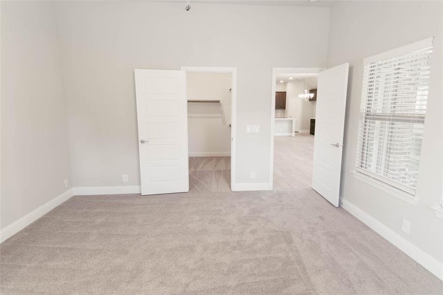 Primary bedroom featuring a walk in closet, light colored carpet, a closet, and a notable chandelier