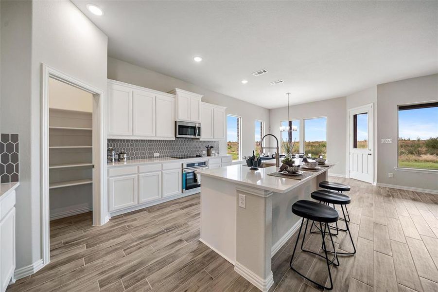 Kitchen with tasteful backsplash, white cabinetry, a breakfast bar area, a chandelier, and a kitchen island with sink Kitchen with tasteful backsplash, white cabinetry, a breakfast bar area, a chandelier, and a kitchen island with sink