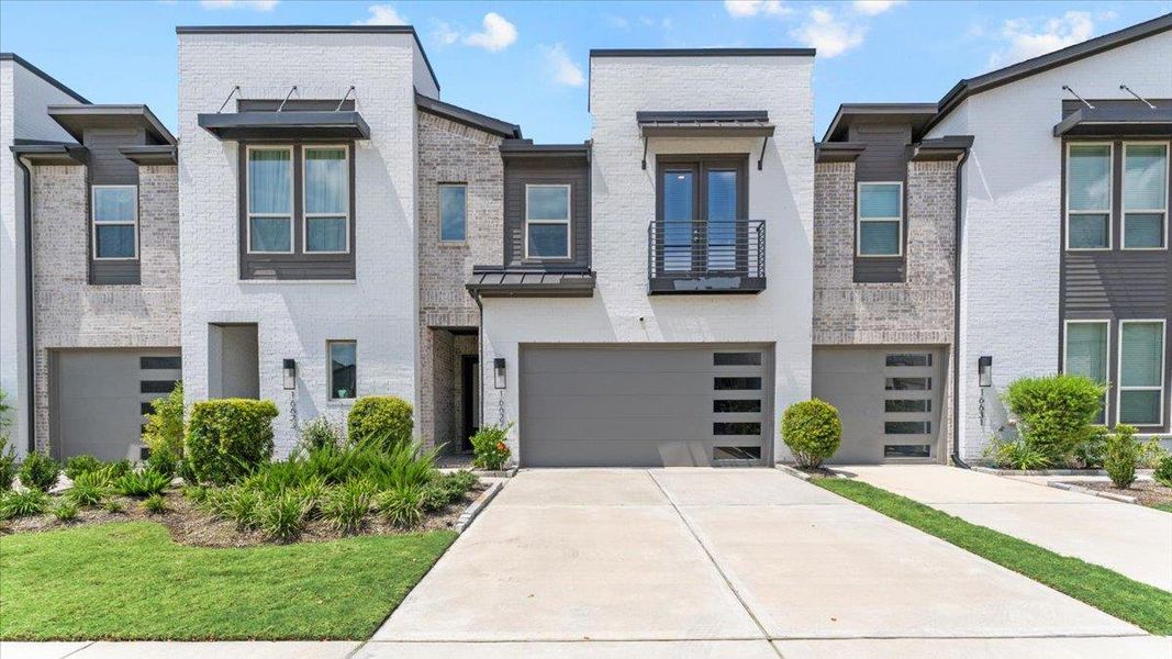 Contemporary home featuring a balcony, driveway, brick siding, a garage, and a standing seam roof Contemporary home featuring a balcony, driveway, brick siding, a garage, and a standing seam roof