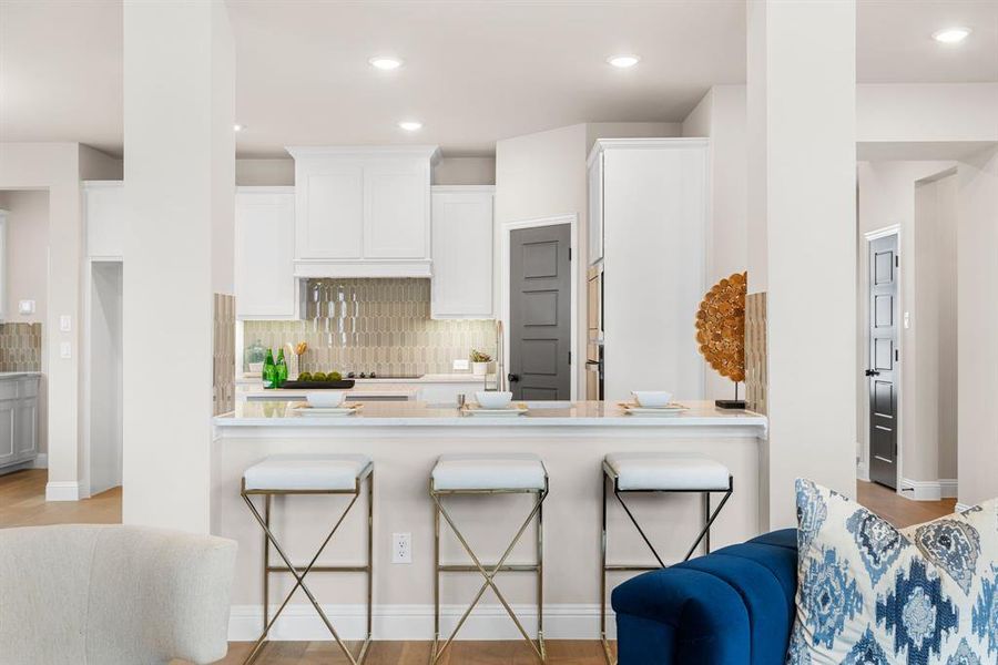 Kitchen with white cabinets, backsplash, light hardwood / wood-style floors, and a breakfast bar