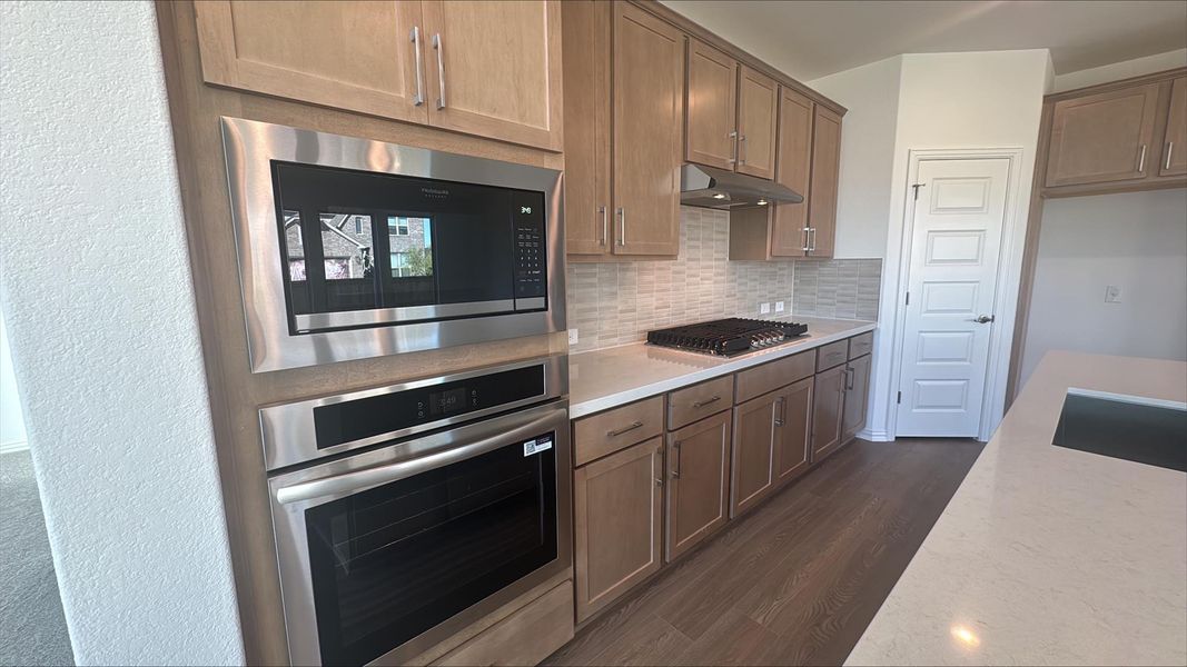 Kitchen with stainless steel appliances, backsplash, dark wood-type flooring, and light stone countertops