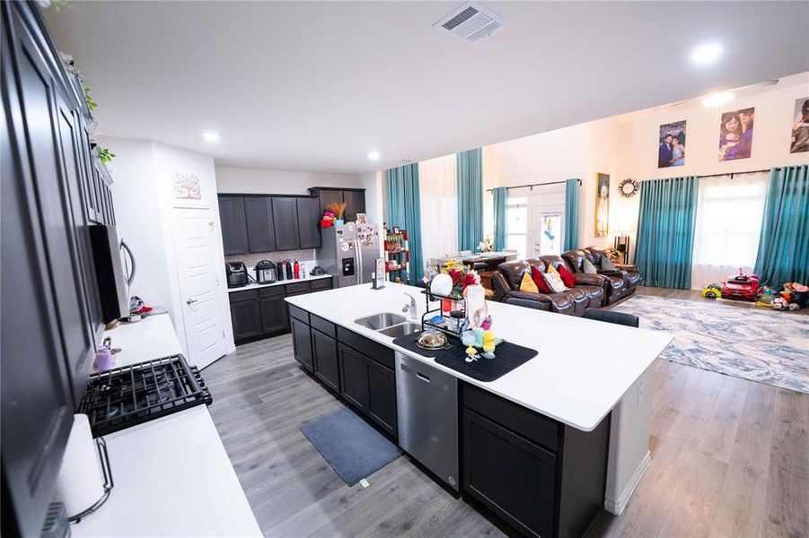 Open-concept living space featuring a kitchen with dark cabinetry, white countertops, and a central island with an undermount sink Open-concept living space featuring a kitchen with dark cabinetry, white countertops, and a central island with an undermount sink