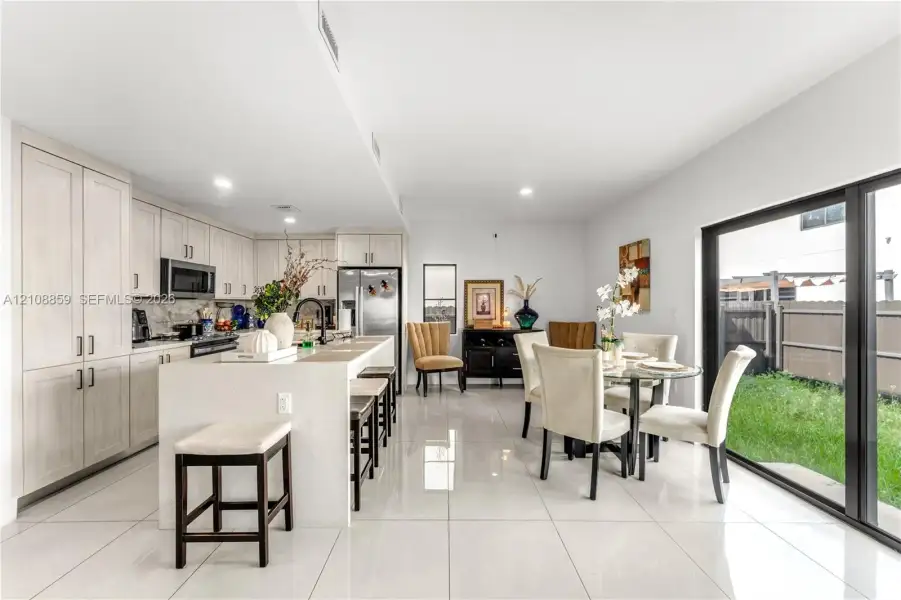 Kitchen featuring light wood-finish cabinetry, a large central island with solid surface countertop, stainless steel appliances, large-format tile flooring, and sliding glass doors leading to the exterior