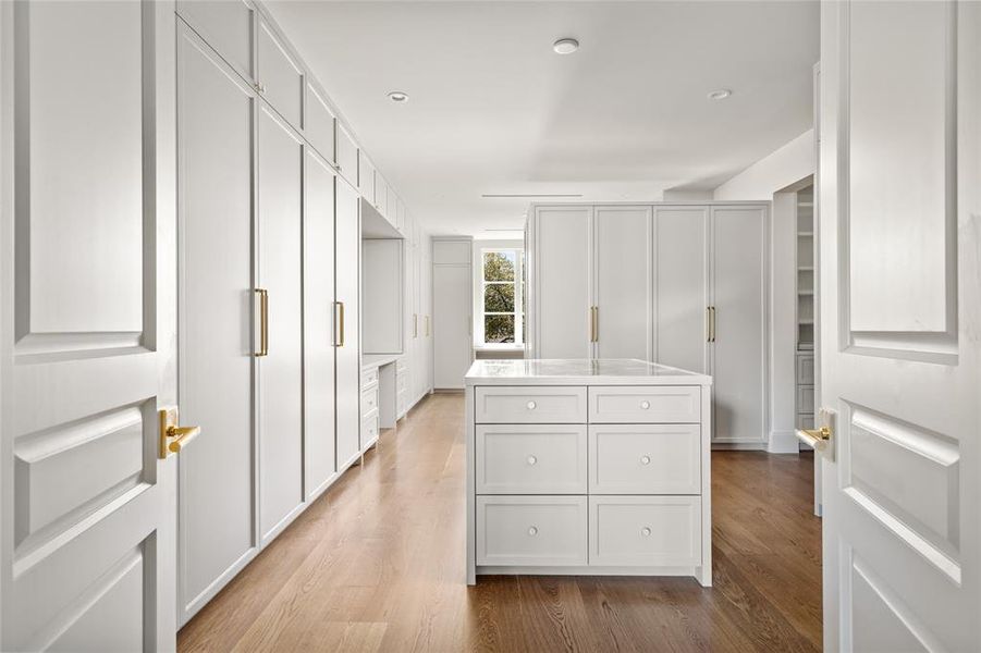 Designed for both luxury and functionality, this expansive primary closet offers custom-built cabinetry, abundant storage, and a central island with an inset mirror top. Large windows provide natural light and serene views, enhancing the airy ambiance.