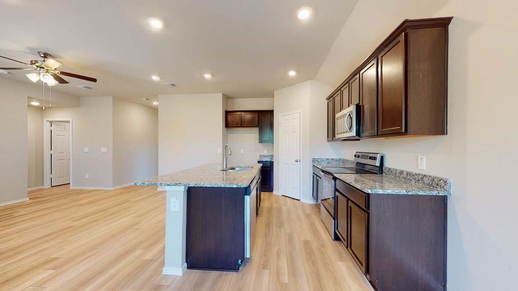 Kitchen featuring an expansive island with a stainless steel sink, granite countertops, dark wood-finish cabinetry, and stainless steel appliances
