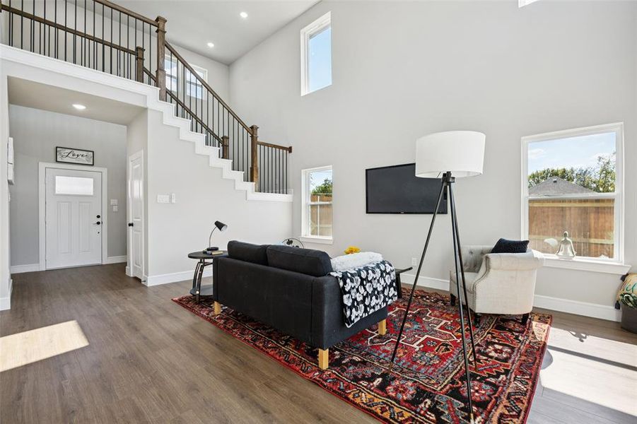 Living room featuring a towering ceiling, healthy amount of natural light, wood finished floors, recessed lighting, and stairway